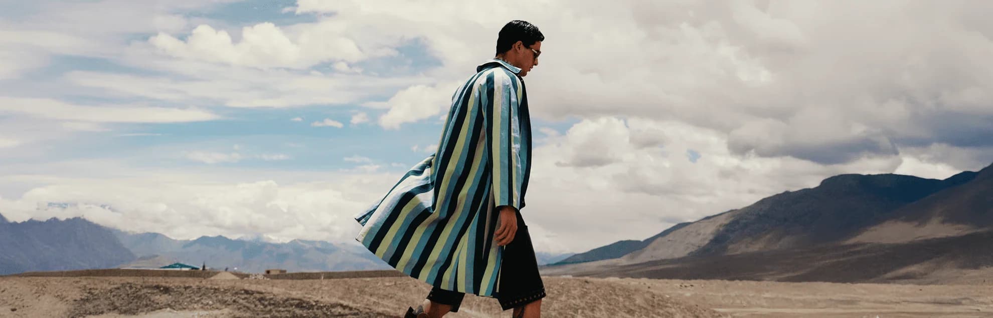 Figure in motion wearing a story-led dress across a lush green landscape